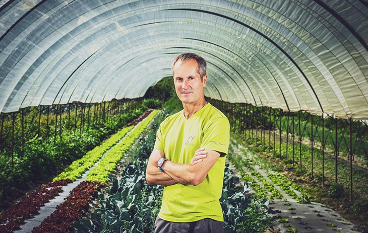Olivier Schupbach Biofruits - Nos producteurs - Une photo d'Olivier Schupbach debout les bras croisés devant une serre de production de légumes biologiques