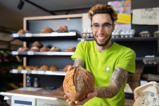 Biofruits - Pain et boulangerie - Une image d'un vendeur Biofruits tendant un pain frais en avant
