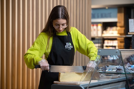 Découpe du fromage au Shop de Vétroz - Une femme dans un magasin découpant un morceau de meule de fromage